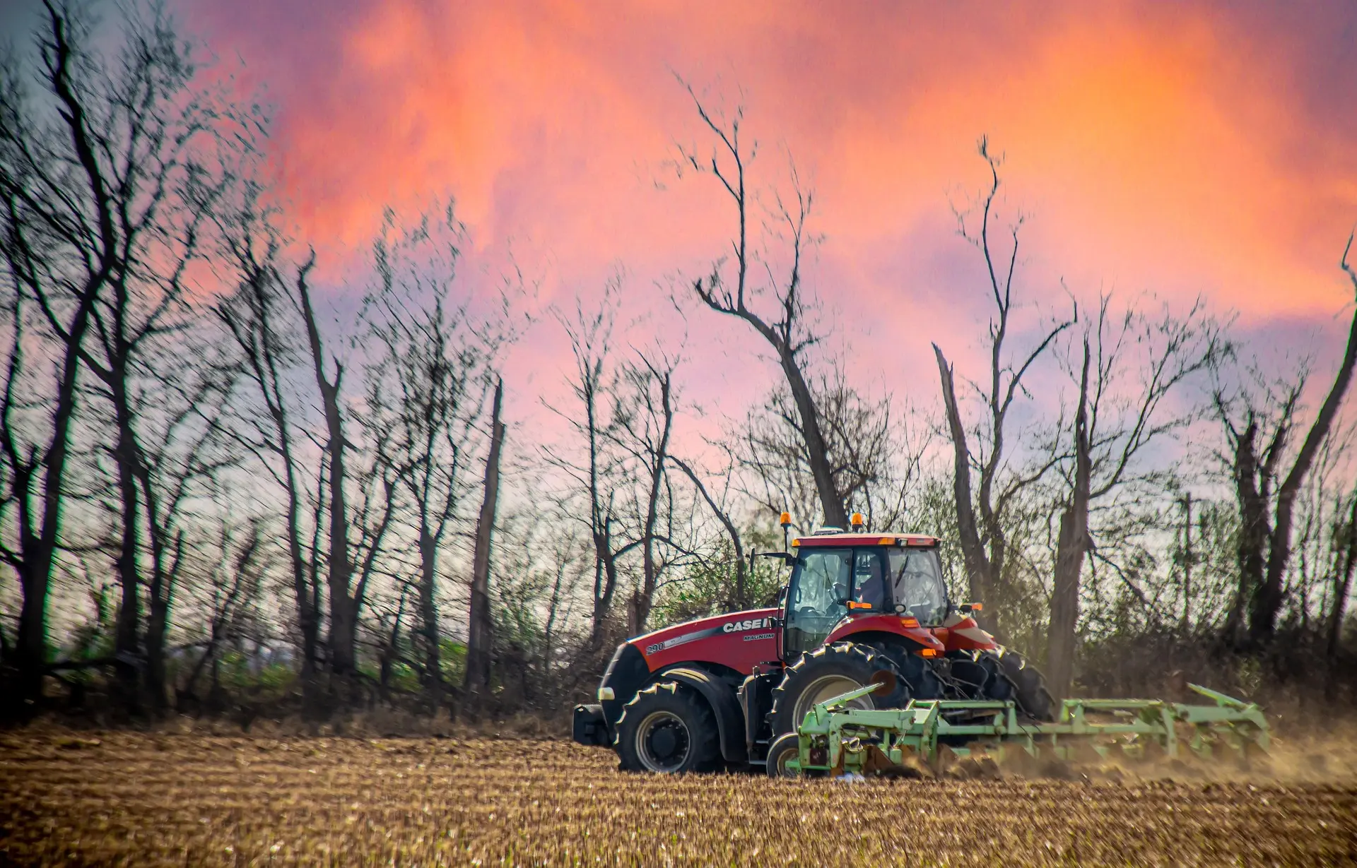 A red CASE tractor works a field at dusk, pulling a green implement under a pink and purple sky. The text "S O R I D E" is visible on the machine.