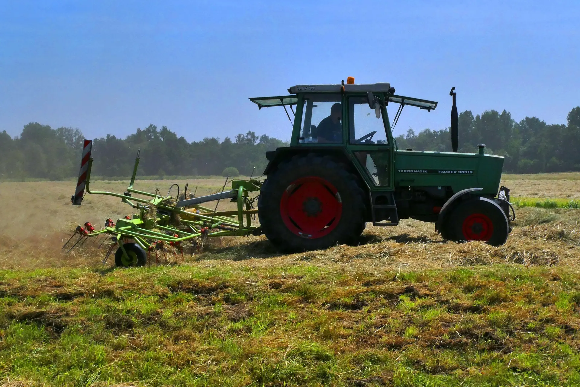 A green tractor with distinctive red wheel rims operates a TURBOMATIK PARKER implement in a golden field, with a driver visible in the cab under a clear blue sky.