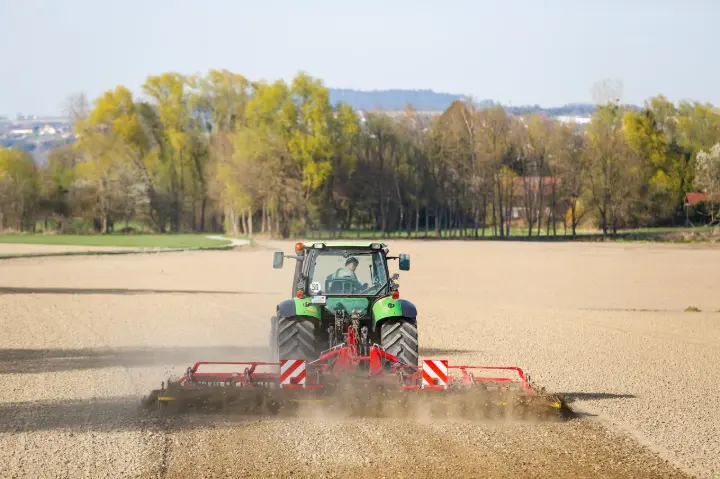 Farmer operating a mid-size tractor with a tiller to plow a field