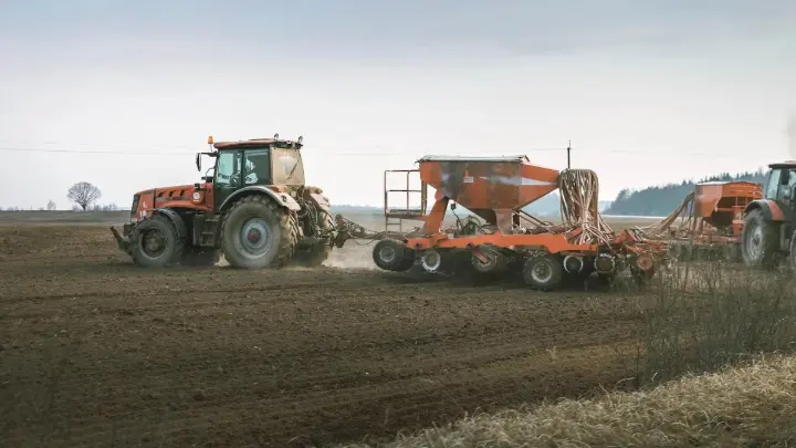 Farmer using a tractor with a seeder to plant crops in a field, showcasing the integration of modern agri software for efficient farm management