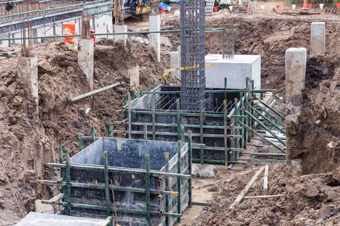 Construction site showing deep excavation and reinforced concrete footings with steel rebar and formwork, illustrating the process of building different types of foundations.