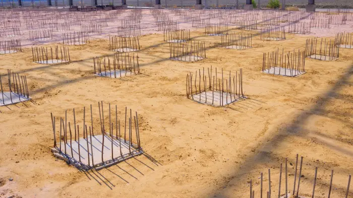 Rows of concrete pad footings with exposed rebar placed in excavated soil, illustrating preparation of shallow foundation types during construction.