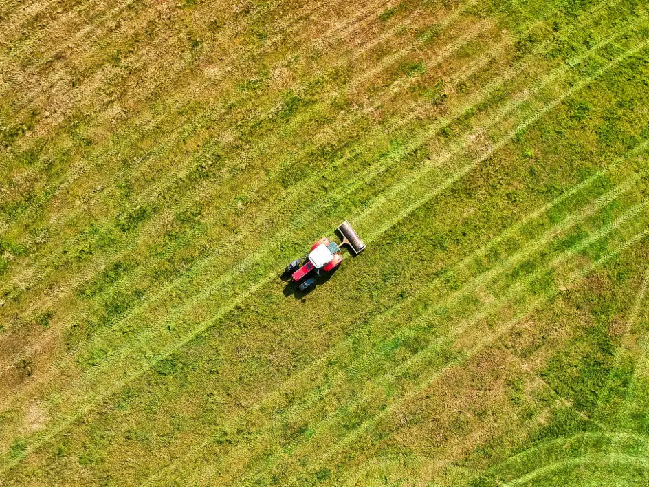 Red tractor mowing green field from above