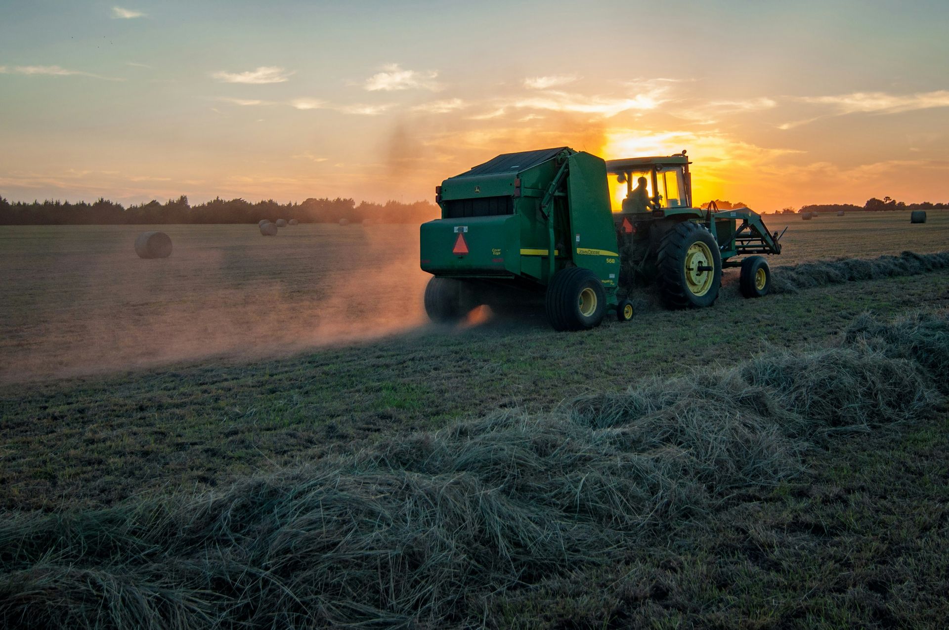 The tractor and baler are harvesting hay.