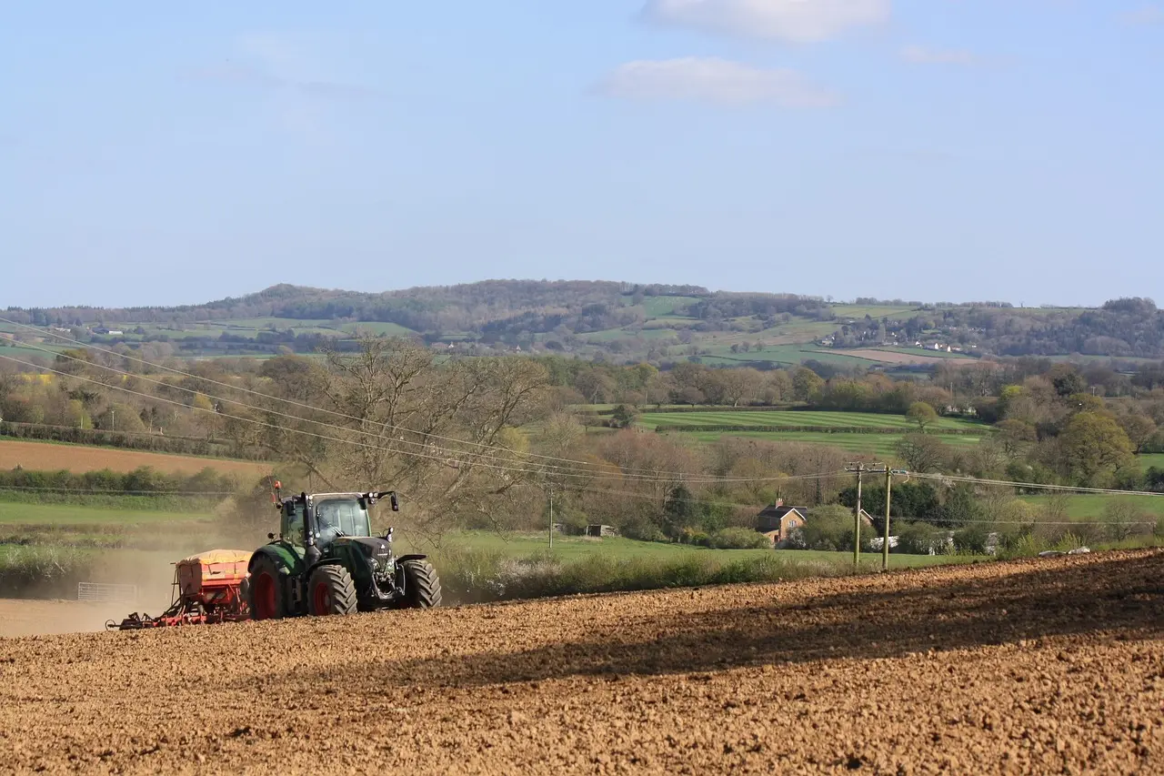 Modern agricultural practice in action: A green tractor prepares a field for planting, showcasing efficient and sustainable soil management amidst a picturesque, tranquil countryside landscape.