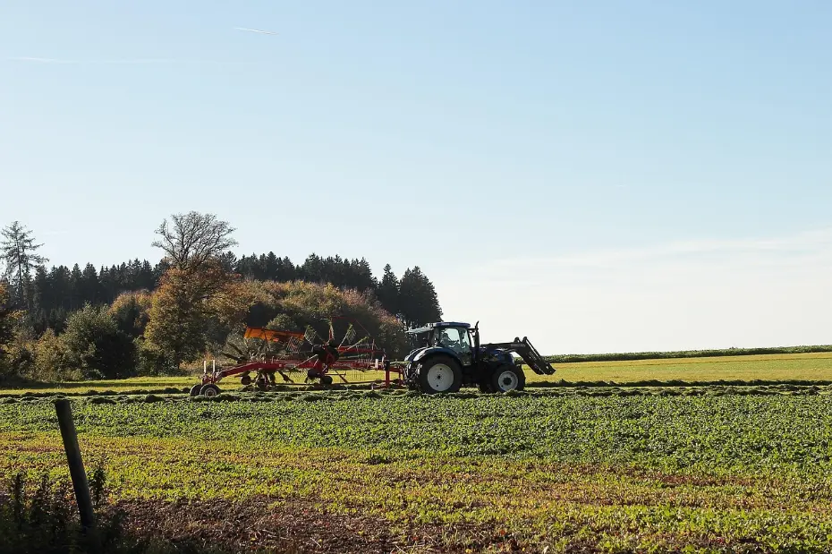 Modern agricultural practice in action: a tractor performs precise field work, symbolizing efficient land management and productivity. The orderly fields and autumn backdrop highlight the harmony between structured farming and the natural seasonal cycle.