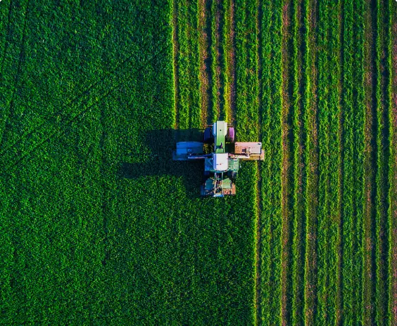 The efficiency of modern agriculture from above: a central piece of farm equipment works within a geometrically precise landscape of green fields. This aerial perspective highlights the machine's role as a core productivity tool within a large-scale, managed, and orderly farming operation.