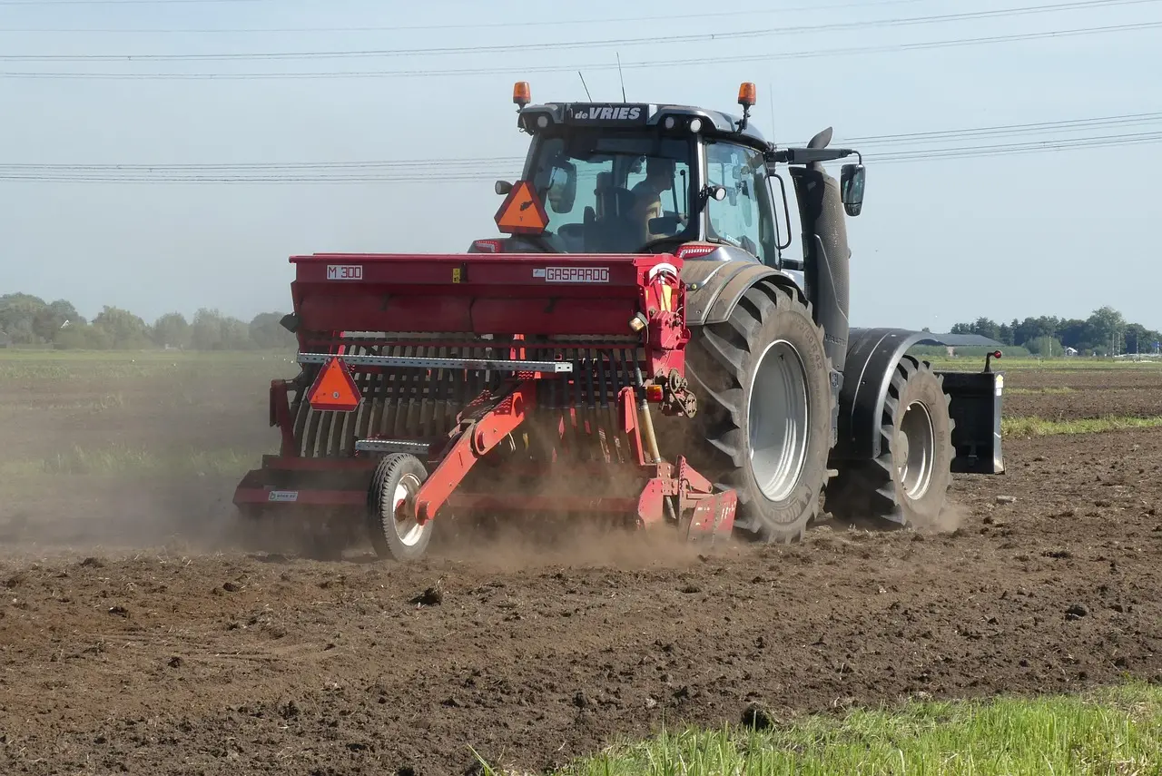 Modern seeding/fertilizing in action: A de VRIES tractor operates a GASPARDO M 300 implement, demonstrating efficient field preparation and input application. The dynamic scene, with dust and contrasting colors, highlights the practical deployment of agricultural equipment.