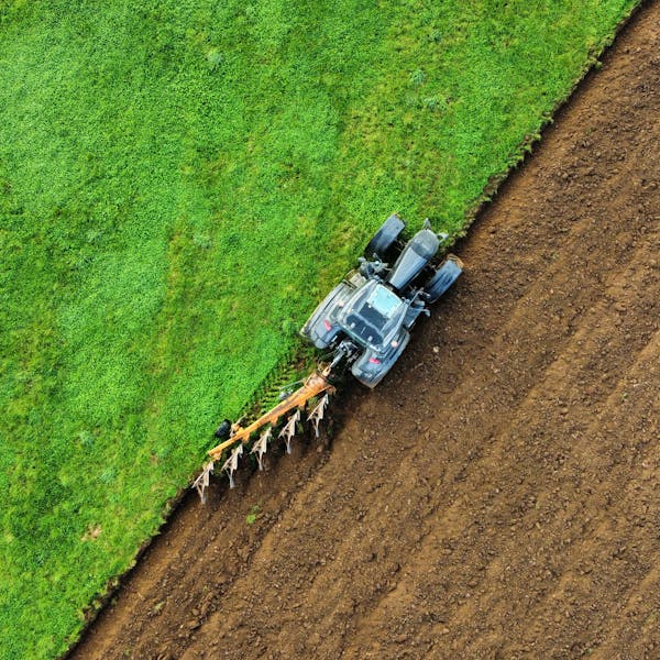 Precision field preparation from above: This aerial shot captures the methodical work of a tractor and plow, vividly showcasing the division between prepared and unprepared land. The image symbolizes the efficiency, scale, and ordered transformation inherent in contemporary mechanized farming.